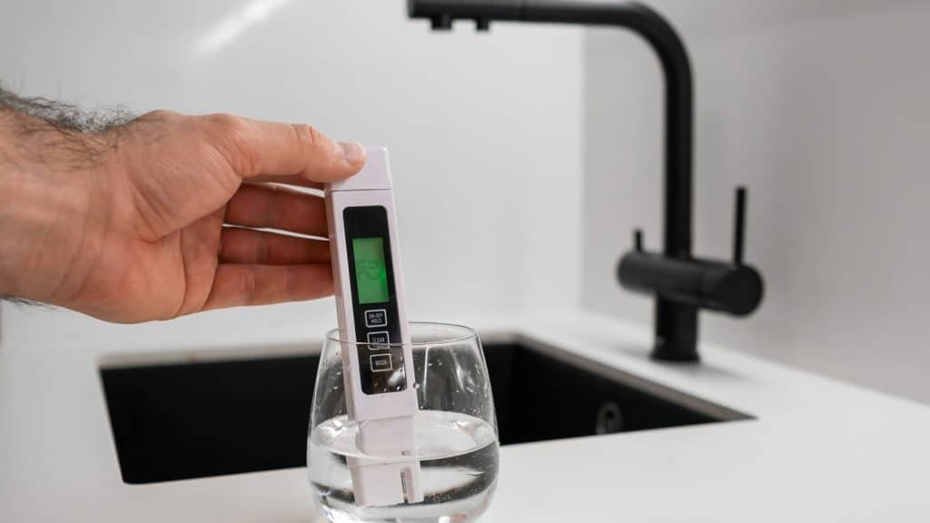 Handheld TDS meter held above a clear glass of water on a kitchen counter